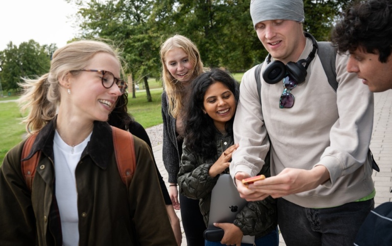 En grupp studenter på campus tittar på en mobil.